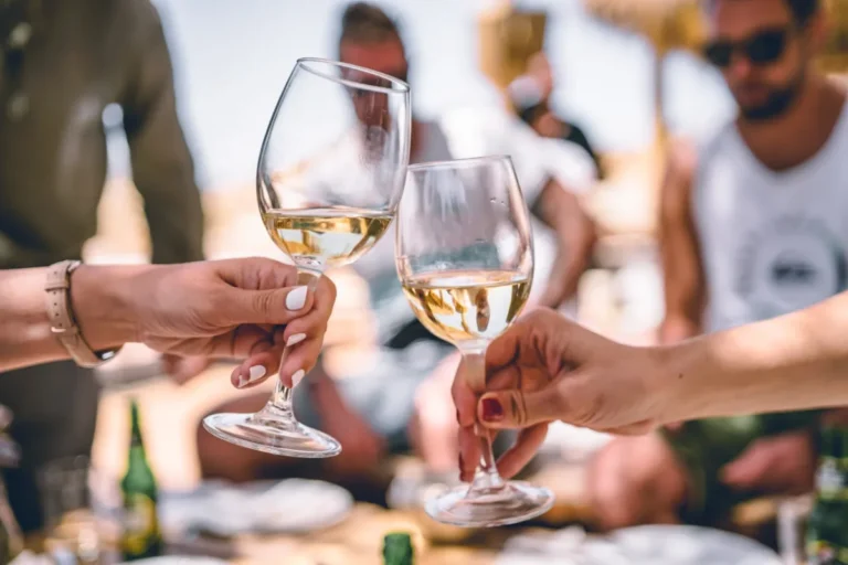 Two people toasting with glasses of white wine outdoors.