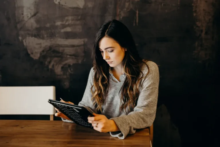 A woman focused on reading a tablet at a wooden table.