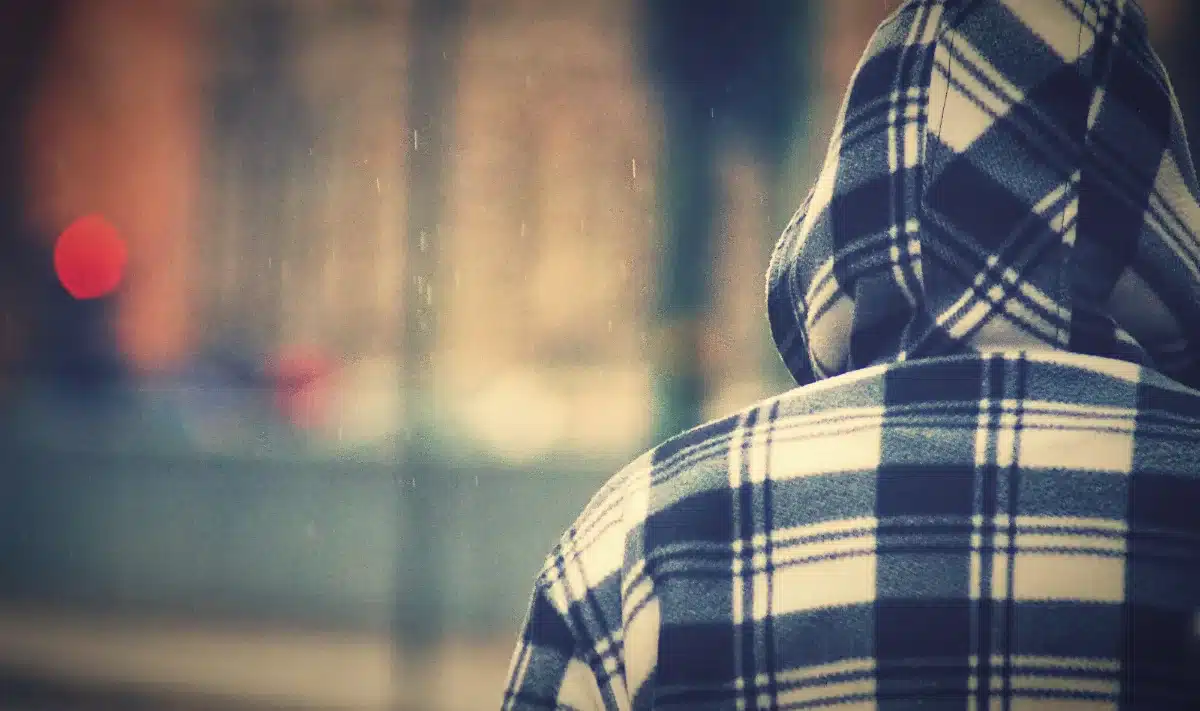 A man wearing a plaid hoodie is walking down the street.