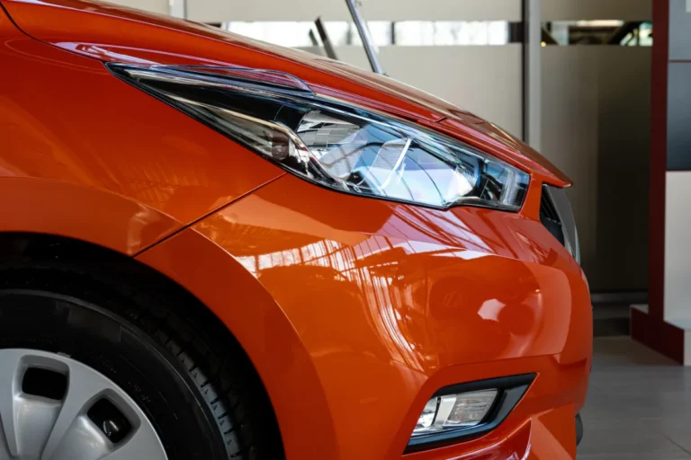 Close-up of an orange car's headlight and front fender design in a showroom.