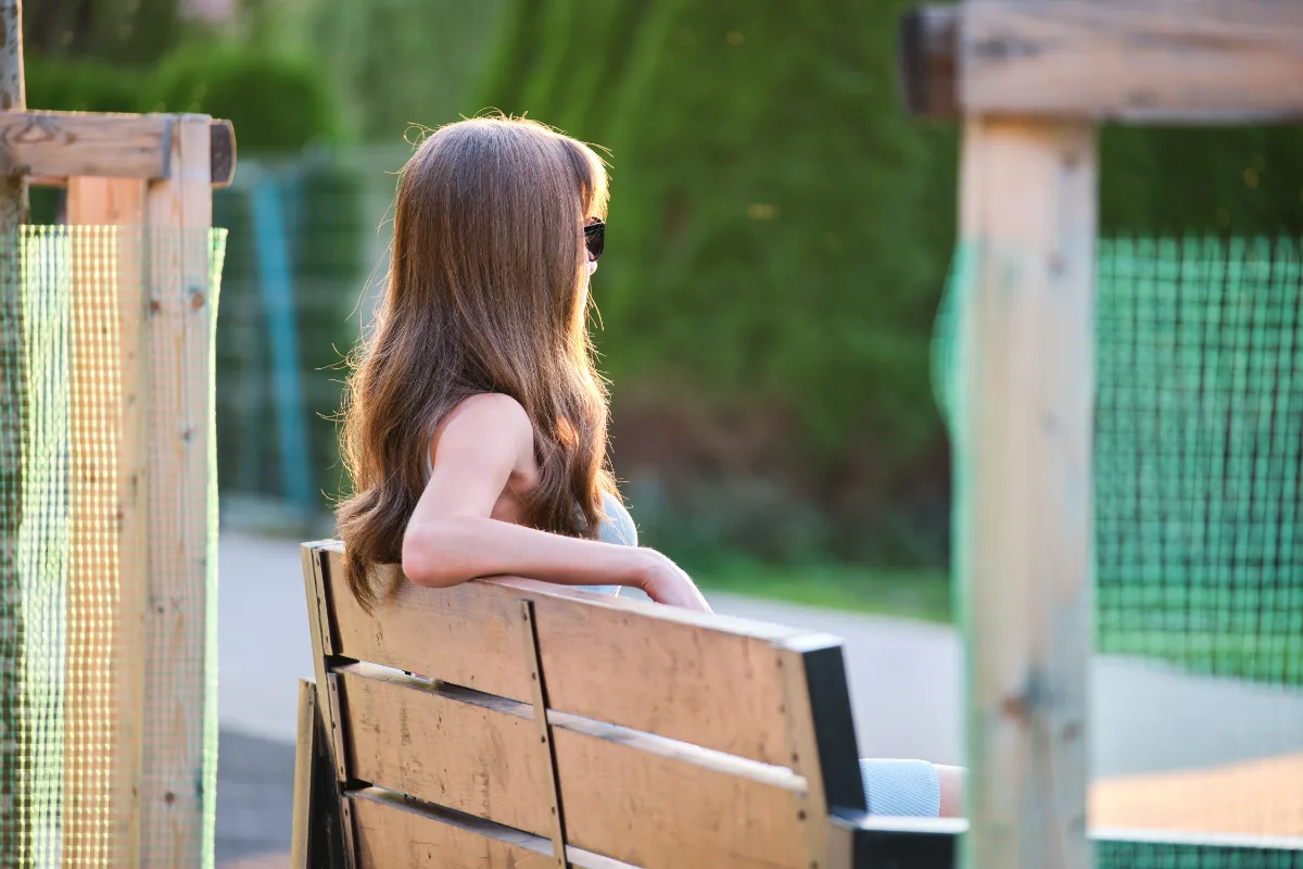 A woman on probation sitting on a bench in a park.