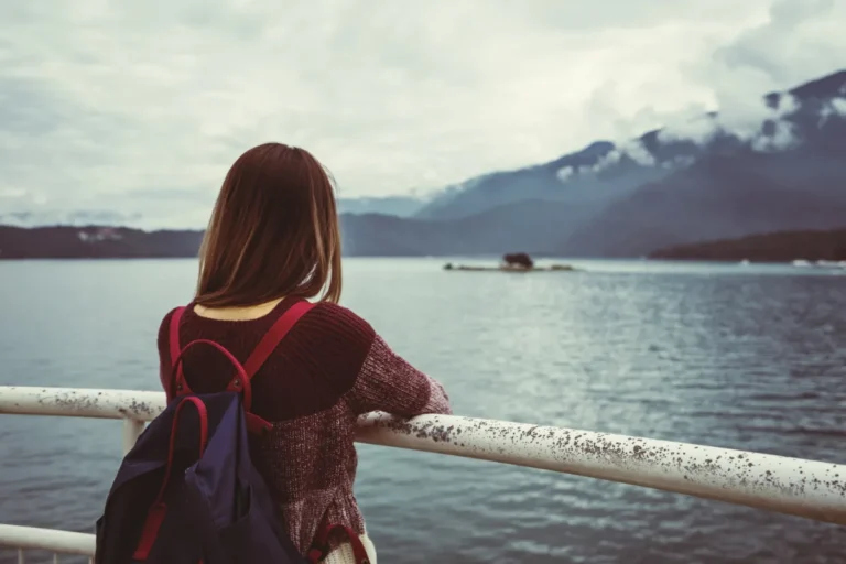 Woman gazing at a mountainous lake landscape from behind a railing.