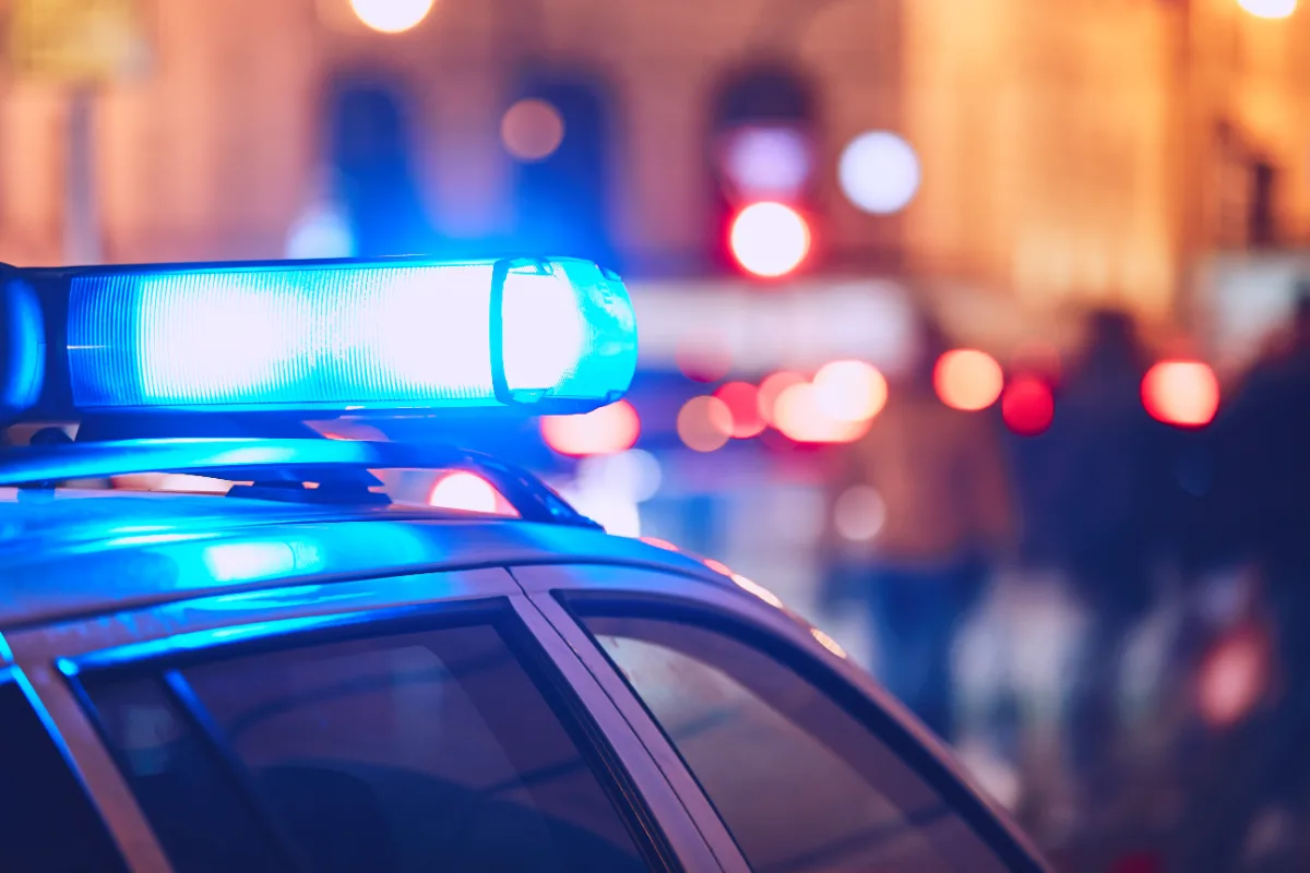 A police car driven by a law enforcement officer patrolling a city street at night.