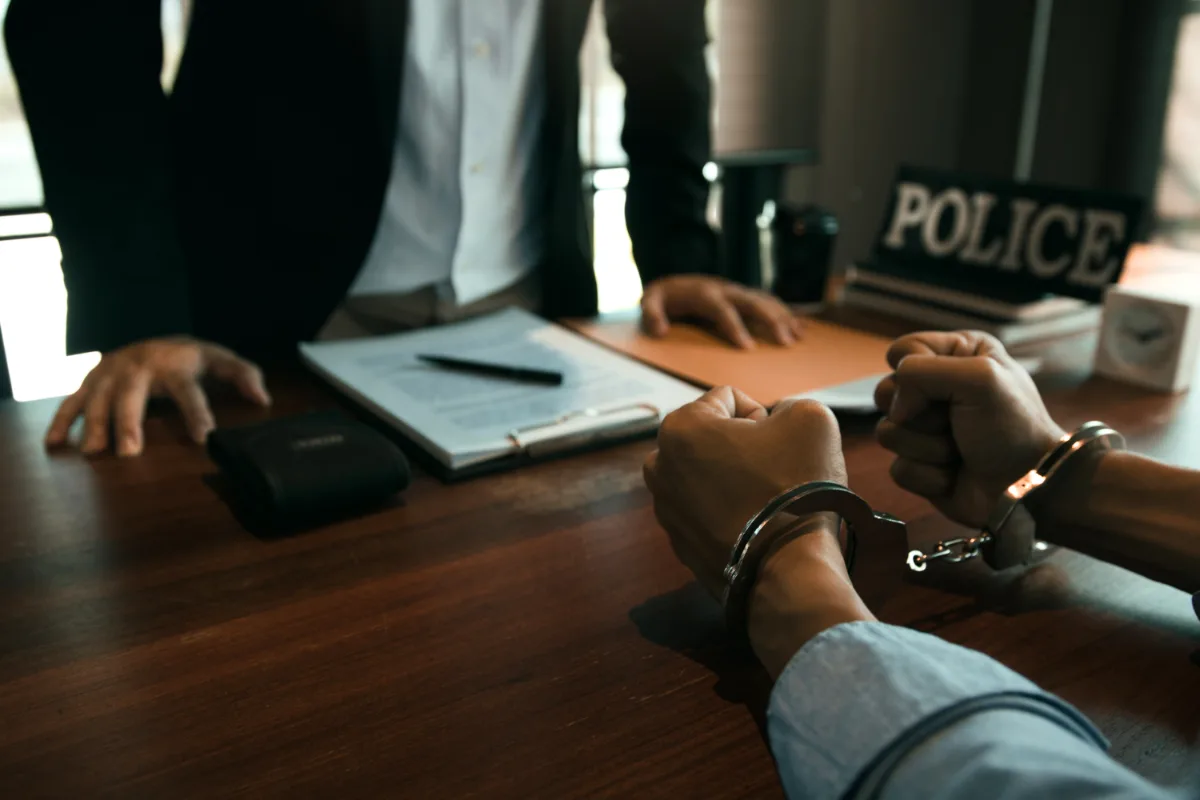 A man with handcuffs in front of a desk, potentially facing misdemeanor charges.