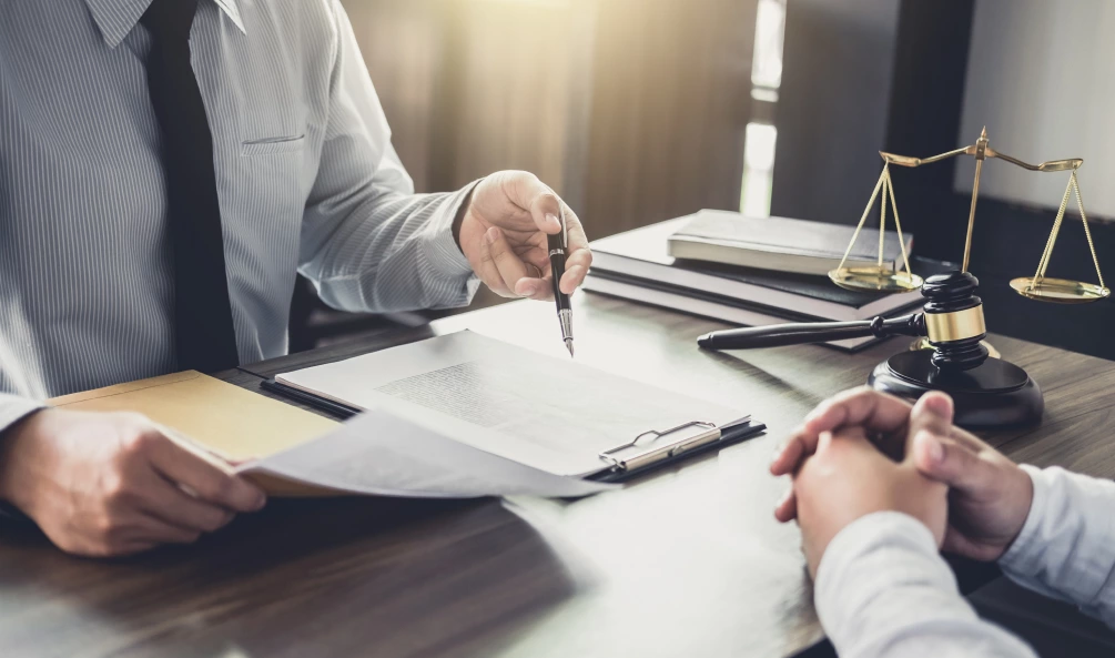 Two people at a desk reviewing legal documents with a gavel and scales of justice in the background.