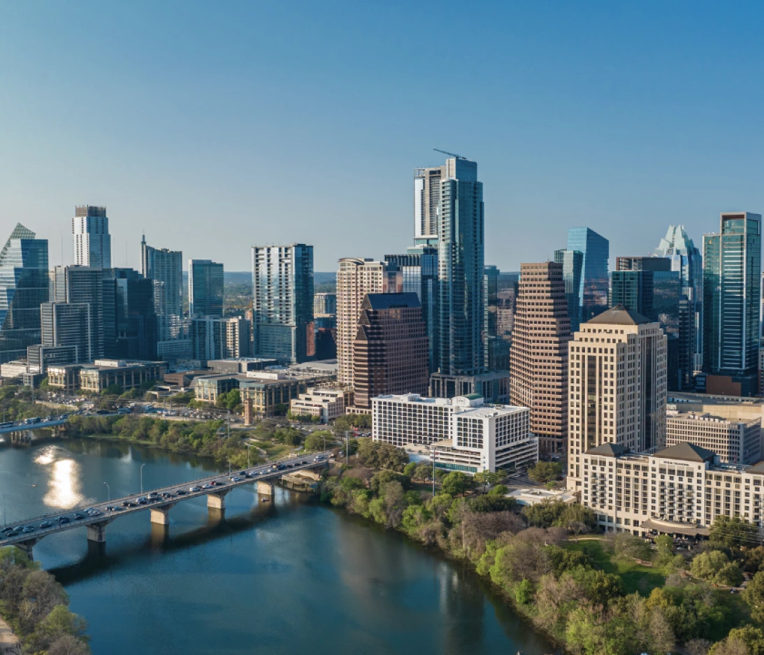 Aerial view of a city skyline featuring numerous modern high-rise buildings, a river, and a bridge with vehicles during the day.