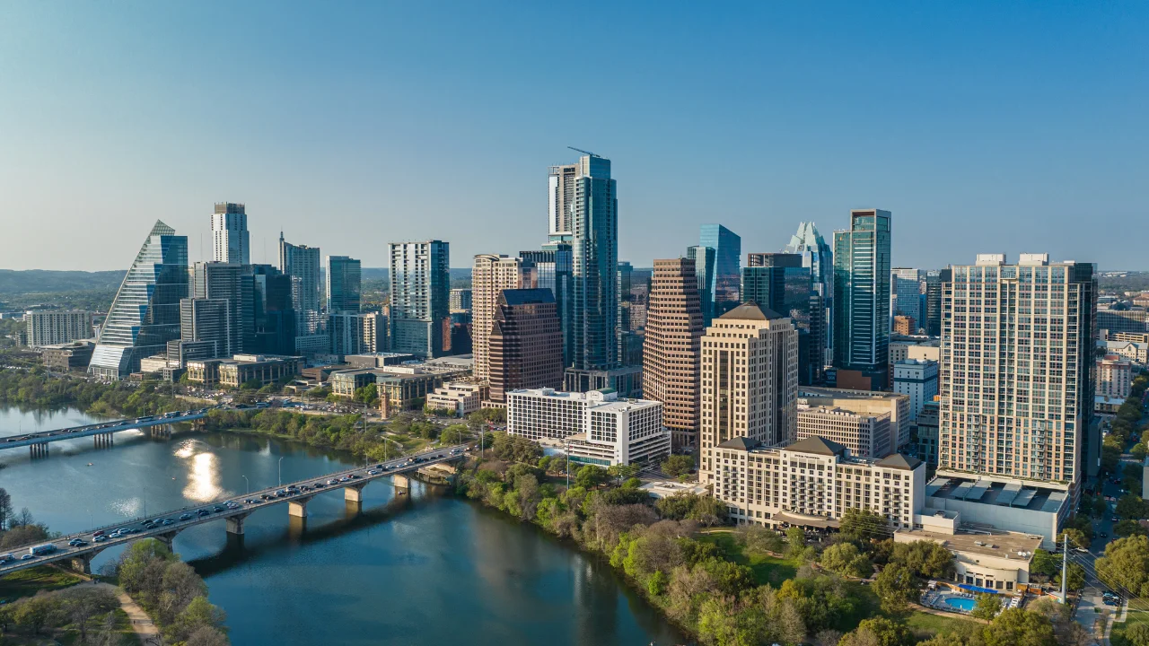 Aerial view of a modern city skyline with high-rise buildings, a river in the foreground, and a bridge crossing the river. The bustling scene is reminiscent of how an Austin DWI Lawyer navigates complex legal landscapes.