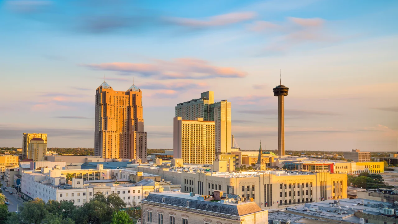 A cityscape of downtown San Antonio, Texas featuring tall buildings, including the Tower of the Americas, against a backdrop of a partly cloudy sky at sunset. Nearby, you might find an Austin DWI Lawyer commuting between these bustling cities.