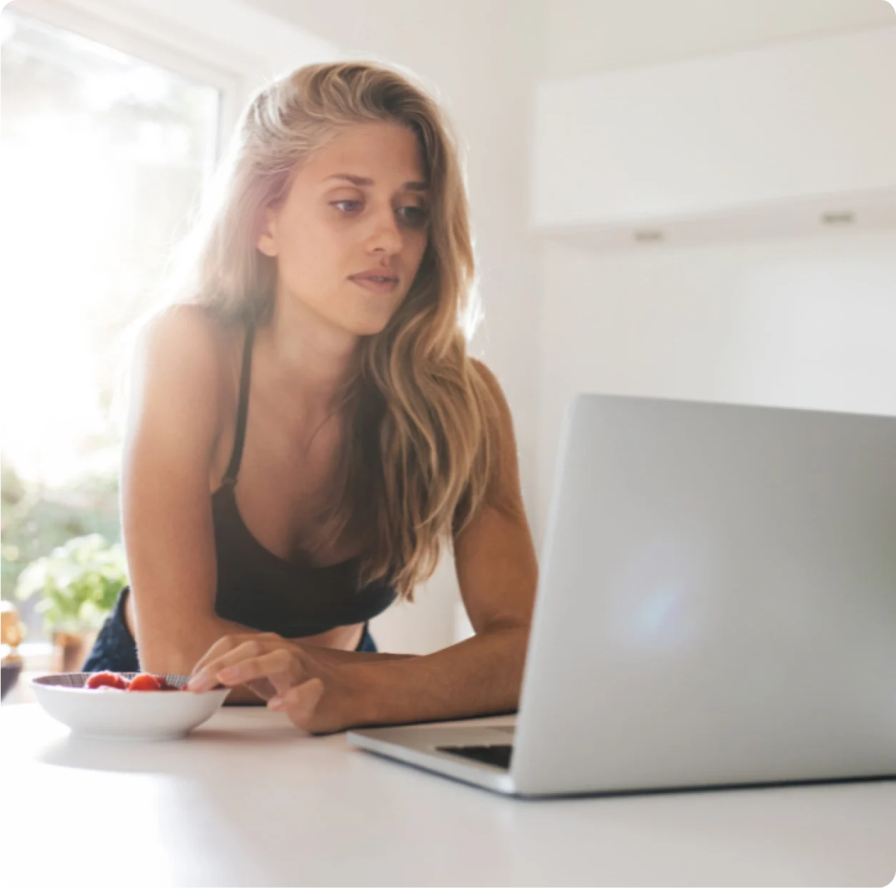 A person with long hair in a black top is using a laptop on a white table, with a bowl of fruit nearby, possibly browsing Texas DWI Attorney Reviews.