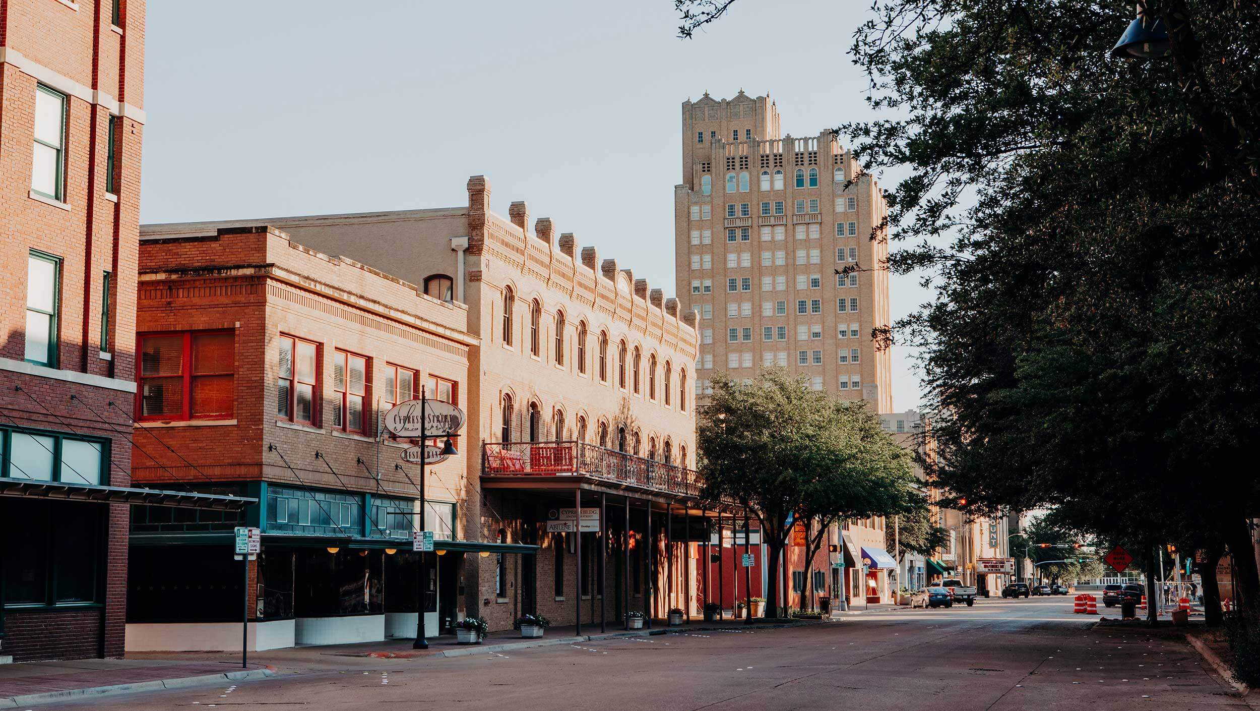 A quiet city street with historic brick buildings and a tall beige tower in the background, reminiscent of where you might find a Abilene Expungement Lawyer. Trees line one side of the street.