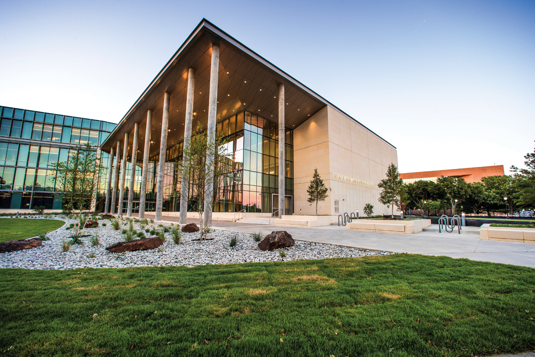 Modern building with large glass windows, tall columns, and a landscaped front area featuring grass and rocks. Under the clear, blue Arlington sky, its design invites peace and reflection amidst the city's vibrant energy.