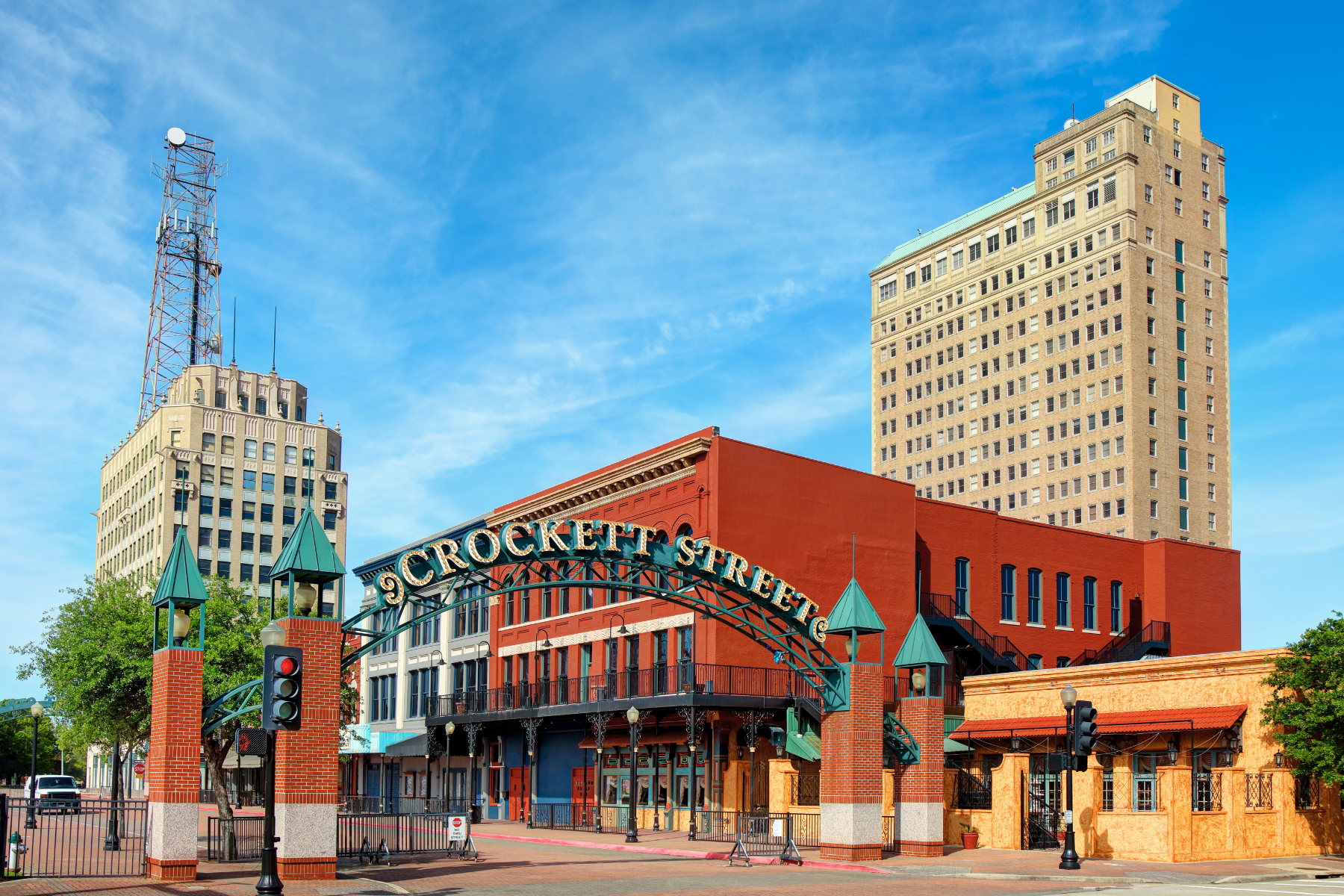 Street view of Crockett Street in Beaumont, Texas, featuring historic buildings, a large arch sign, and two tall towers under a clear blue sky—a perfect spot to discuss your case with an Beaumont expungement lawyer.