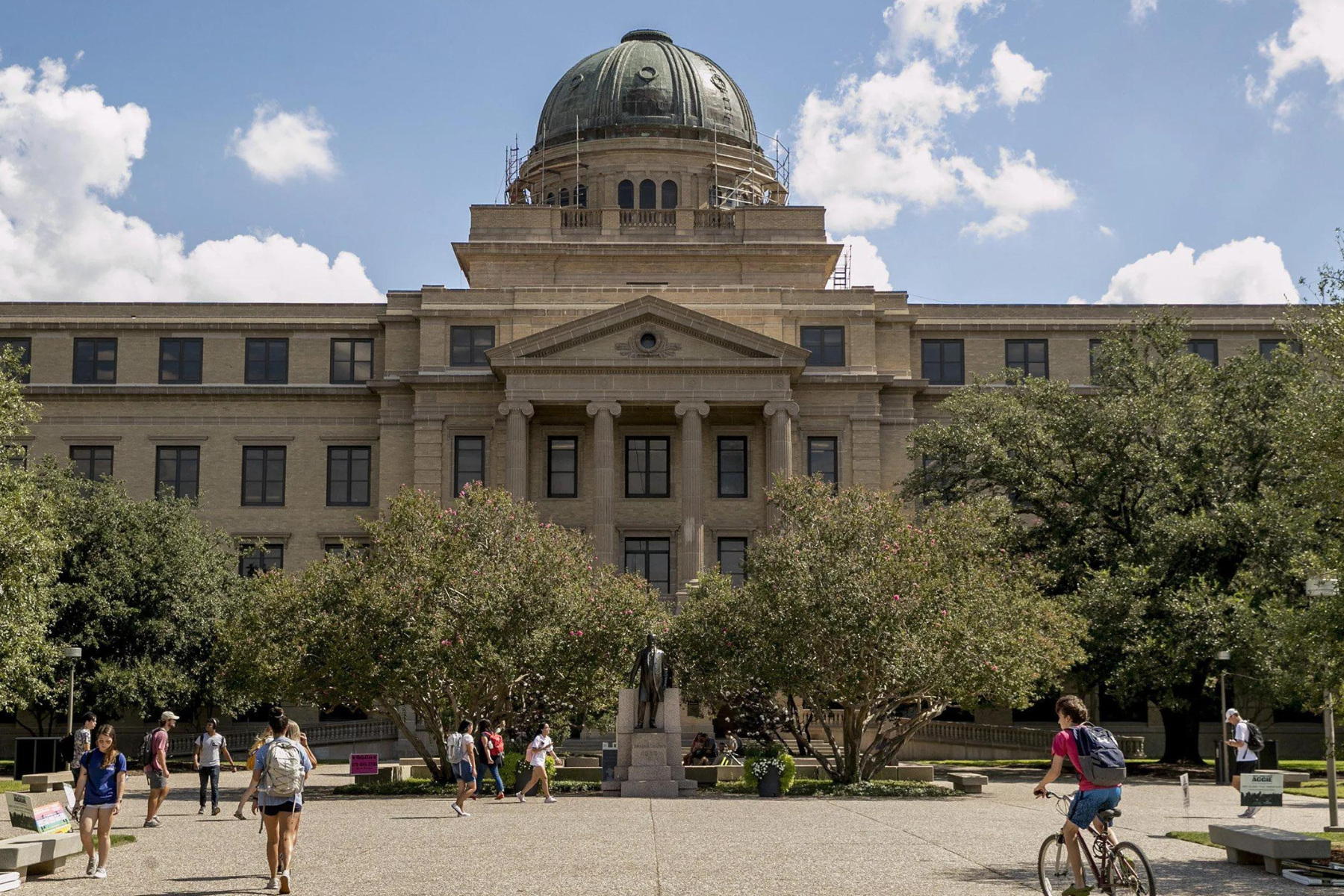 The university building with its domed roof is surrounded by lush trees, creating a peaceful atmosphere where people, including a few College Station expungement lawyers taking a break from work, walk and bike through the bustling courtyard.