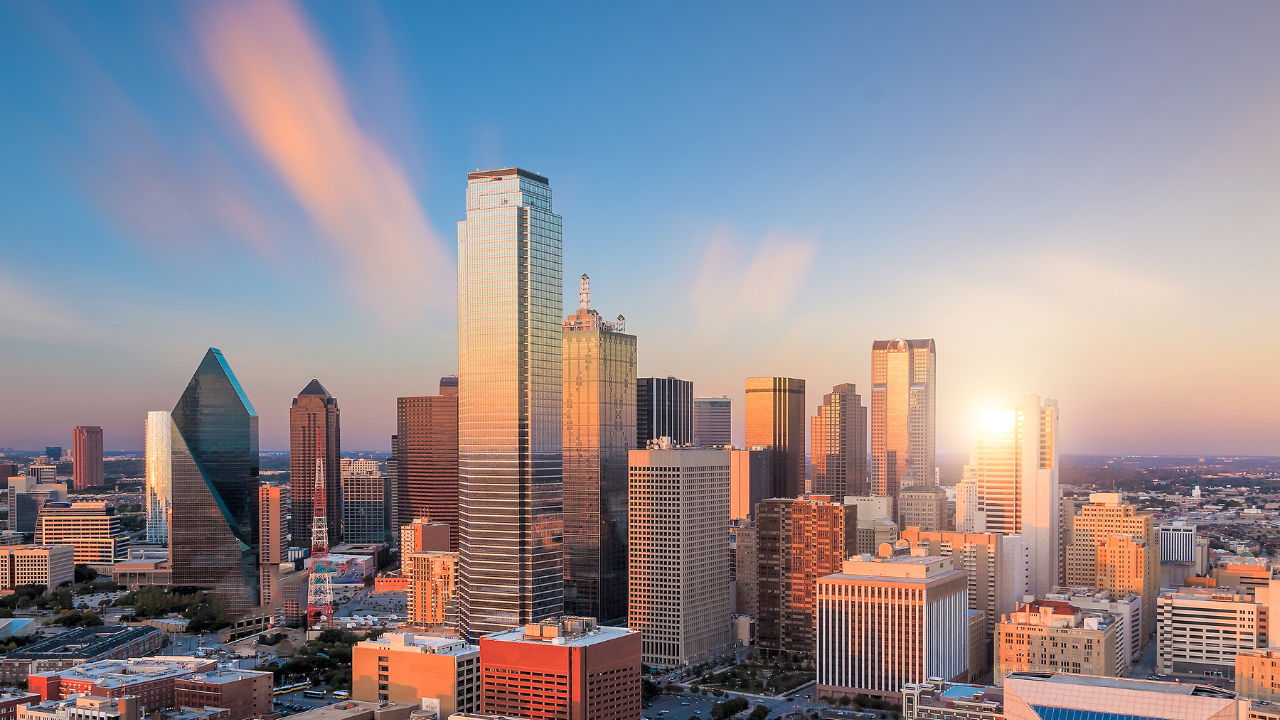 Aerial view of Dallas' city skyline at sunset, featuring tall skyscrapers with glass facades reflecting the orange and pink hues of the sky—an inspiring scene as you ponder finding a trusted Dallas DWI Lawyer amidst this urban beauty.