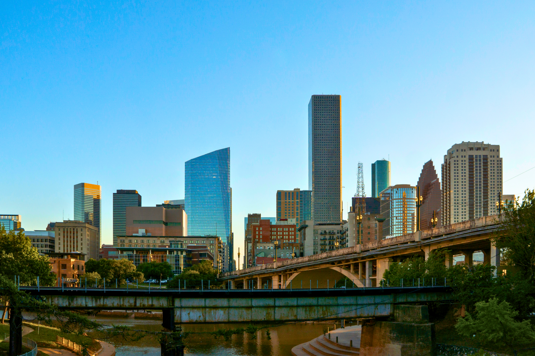 The city skyline with modern buildings and a bridge in the foreground stretches against a clear blue sky, echoing the vibrant energy of Houston, where even finding a public intoxication lawyer is just another part of its bustling urban life.