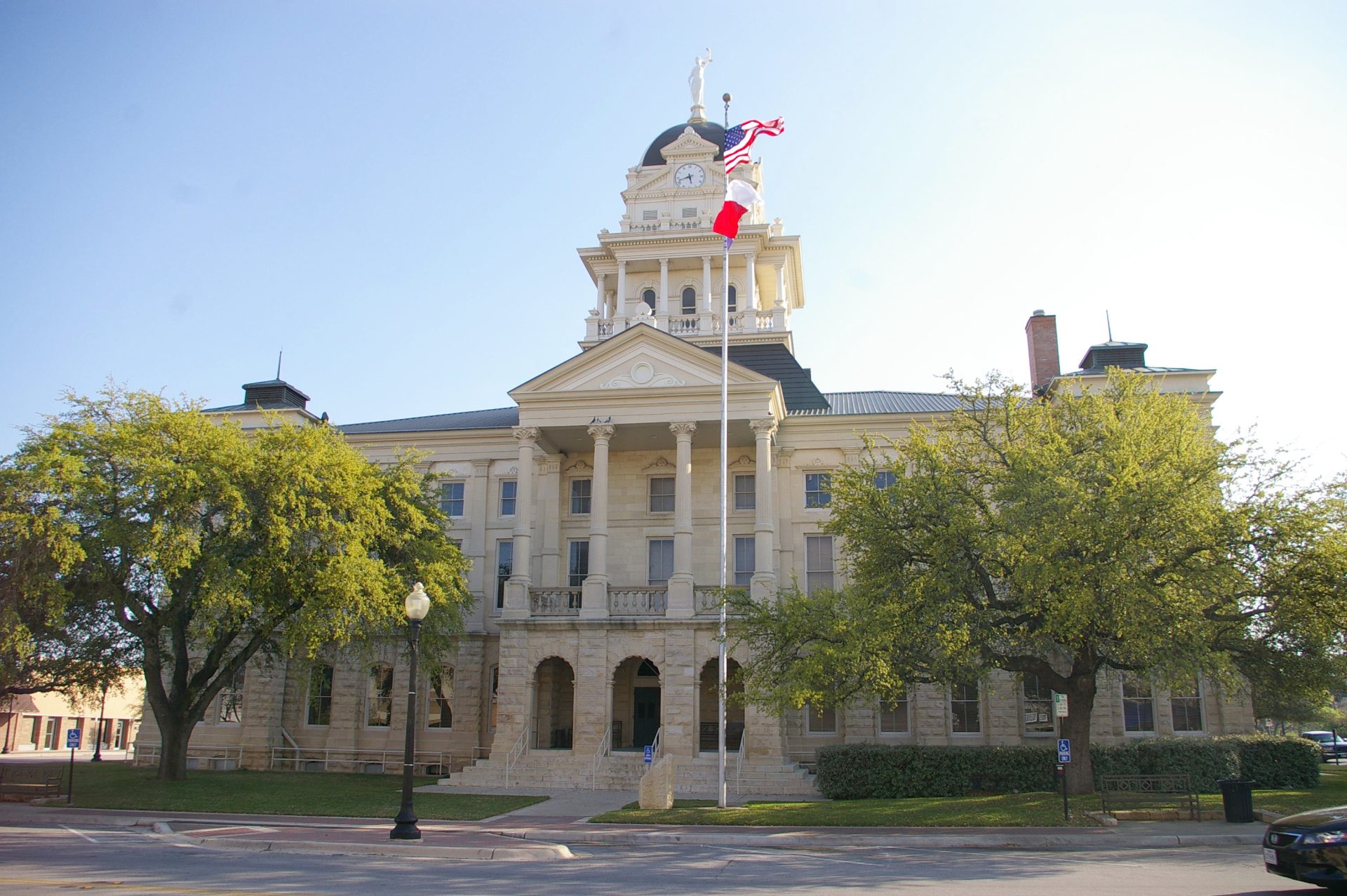 A historic building with a clock tower and columns stands surrounded by trees, reminiscent of the esteemed architecture where a Killeen expungement lawyer might practice. Two flags are on poles in front, adding to its distinguished presence.