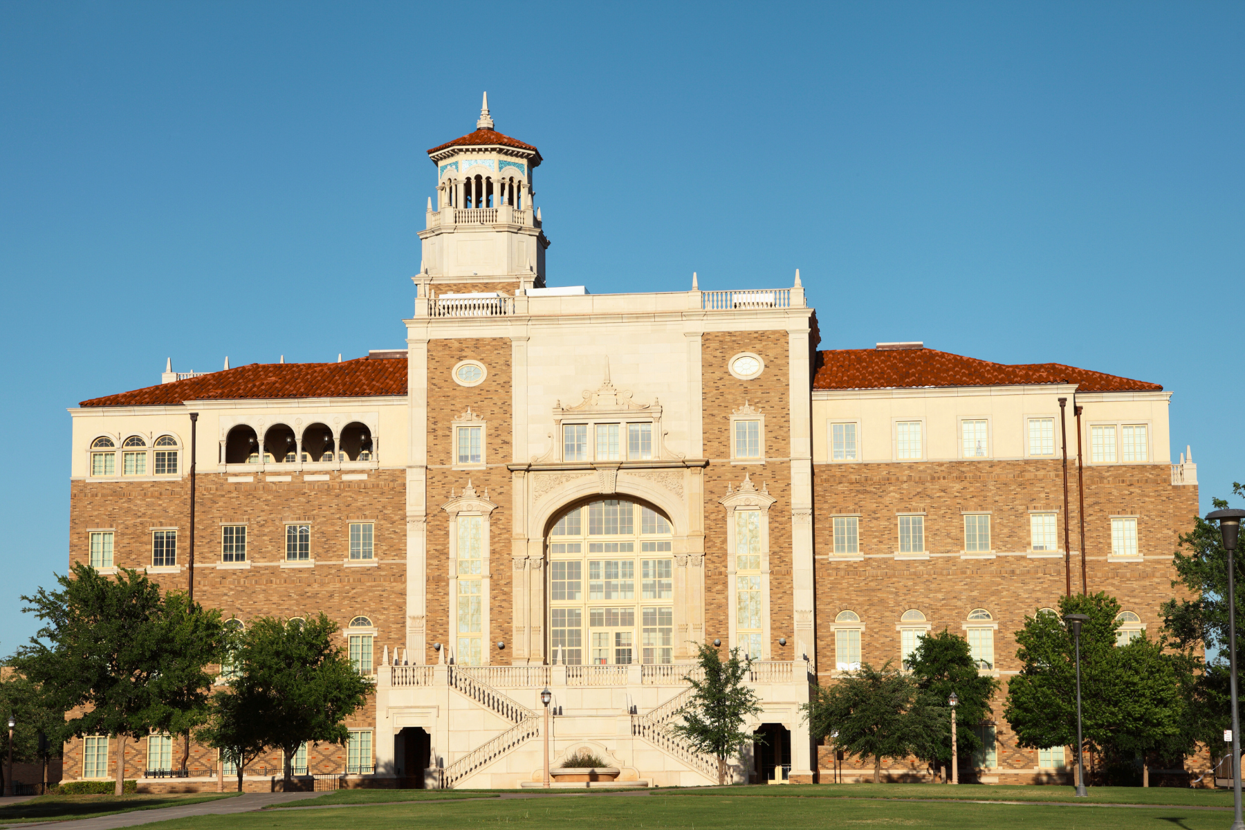 A large brick and stone building with a central tower, arched windows, and a grand staircase evokes the stature of a Lubbock Expungement Lawyer under the clear blue sky.