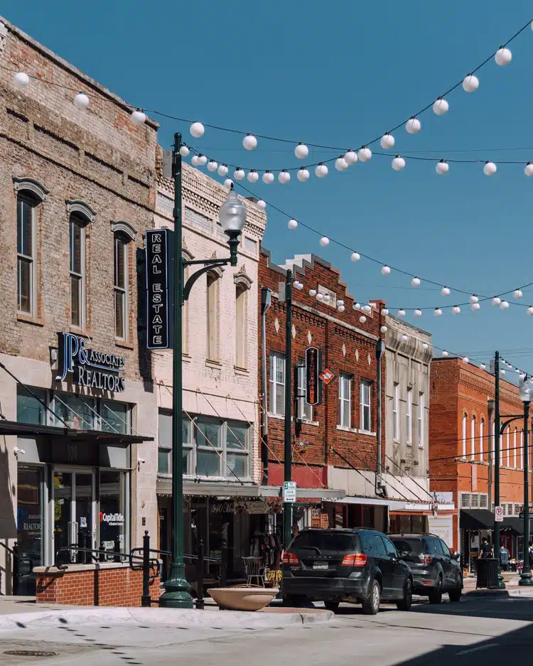 A small-town street with brick buildings, parked cars, and string lights hanging above offers charm and simplicity, much like finding the right McKinney expungement lawyer to guide you through clearing past mistakes for a brighter future.