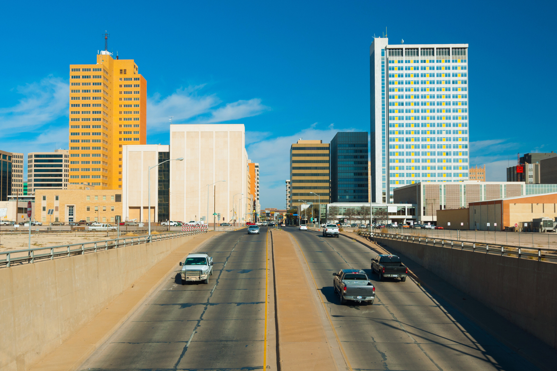 A wide road bustling with cars leads into a cityscape of towering buildings under a clear blue sky, reminiscent of the clarity one might seek from a skilled Midland expungement lawyer.