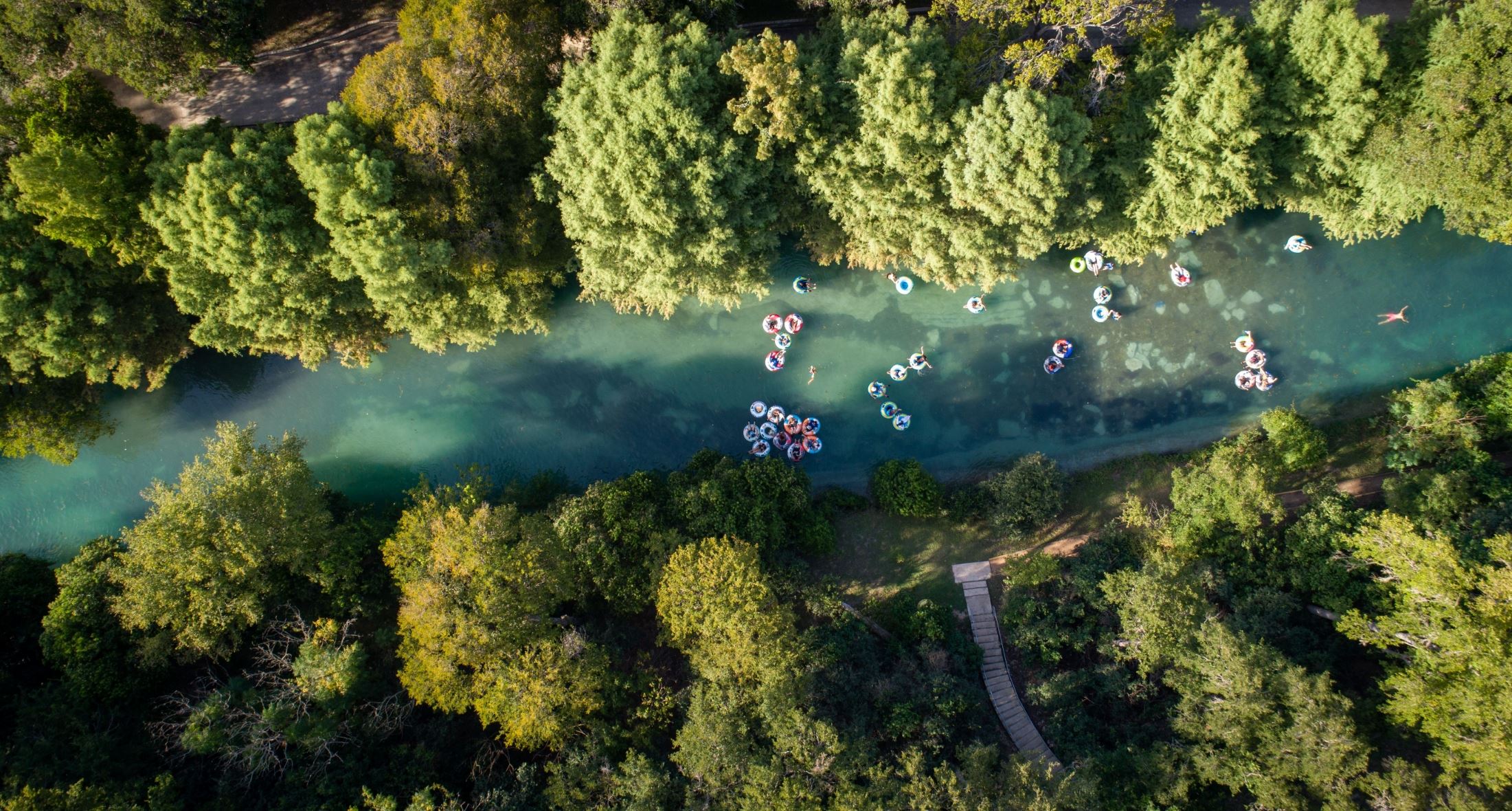 An aerial view of a river surrounded by dense green trees showcases people floating on inflatable tubes, their carefree afternoon resembling the calm after a New Braunfels expungement lawyer resolves a case.