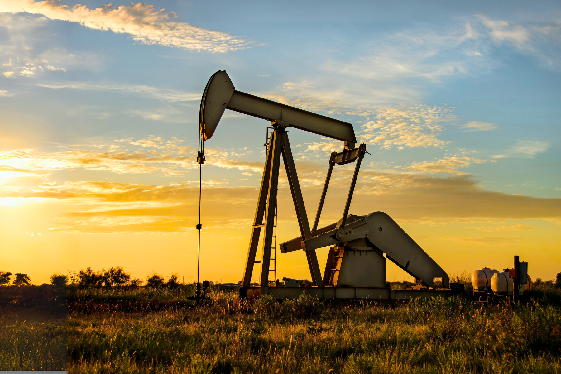 An oil pumpjack operates in a grassy field at sunset, painting the horizon with hues of gold and orange. The scene is as meticulously crafted as a Odessa expungement lawyer's attention to detail, set against a partly cloudy sky that adds depth and intrigue.