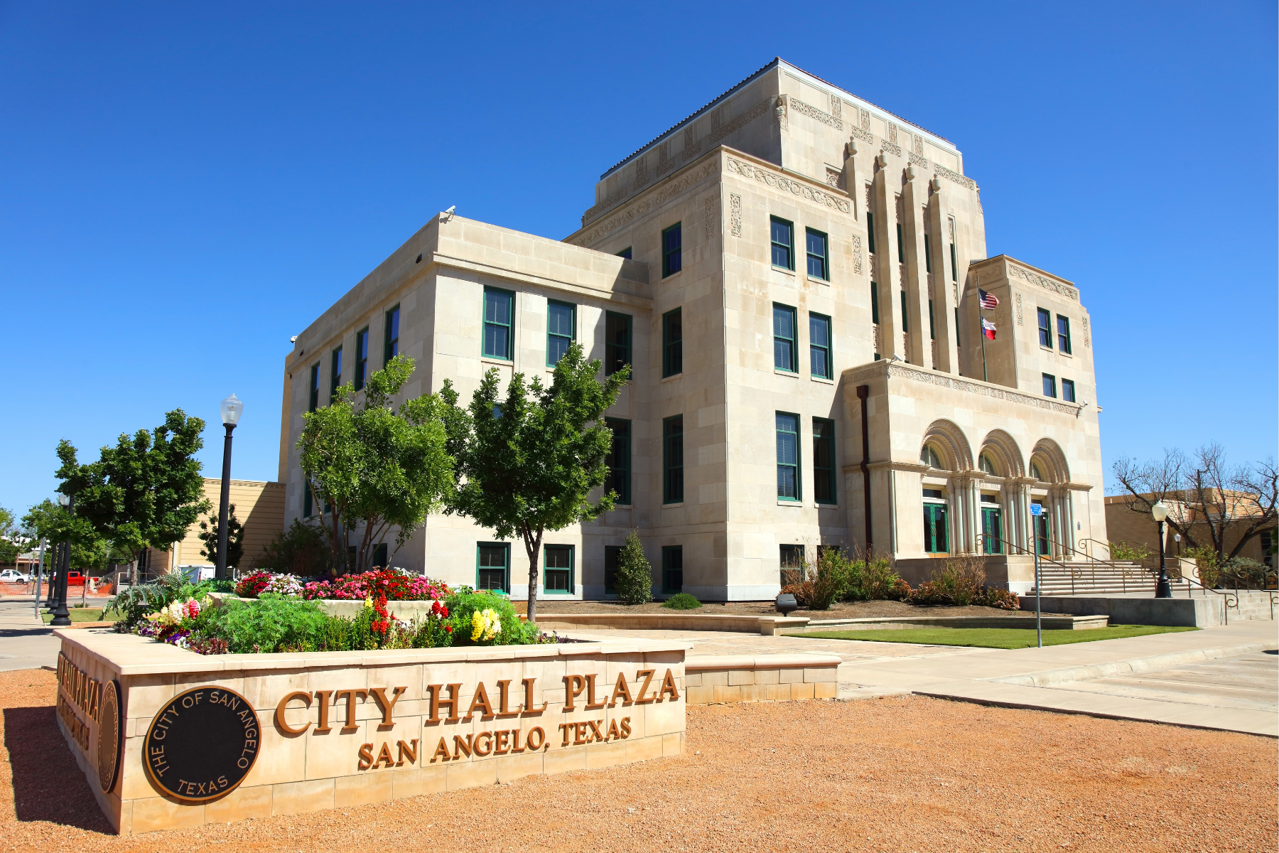 City Hall Plaza in San Angelo, Texas, features a stunning beige stone building surrounded by beautifully landscaped flowers and a prominent sign in the foreground. Just like the meticulous work of a San Angelo expungement lawyer, every detail is thoughtfully considered to create an impressive view.