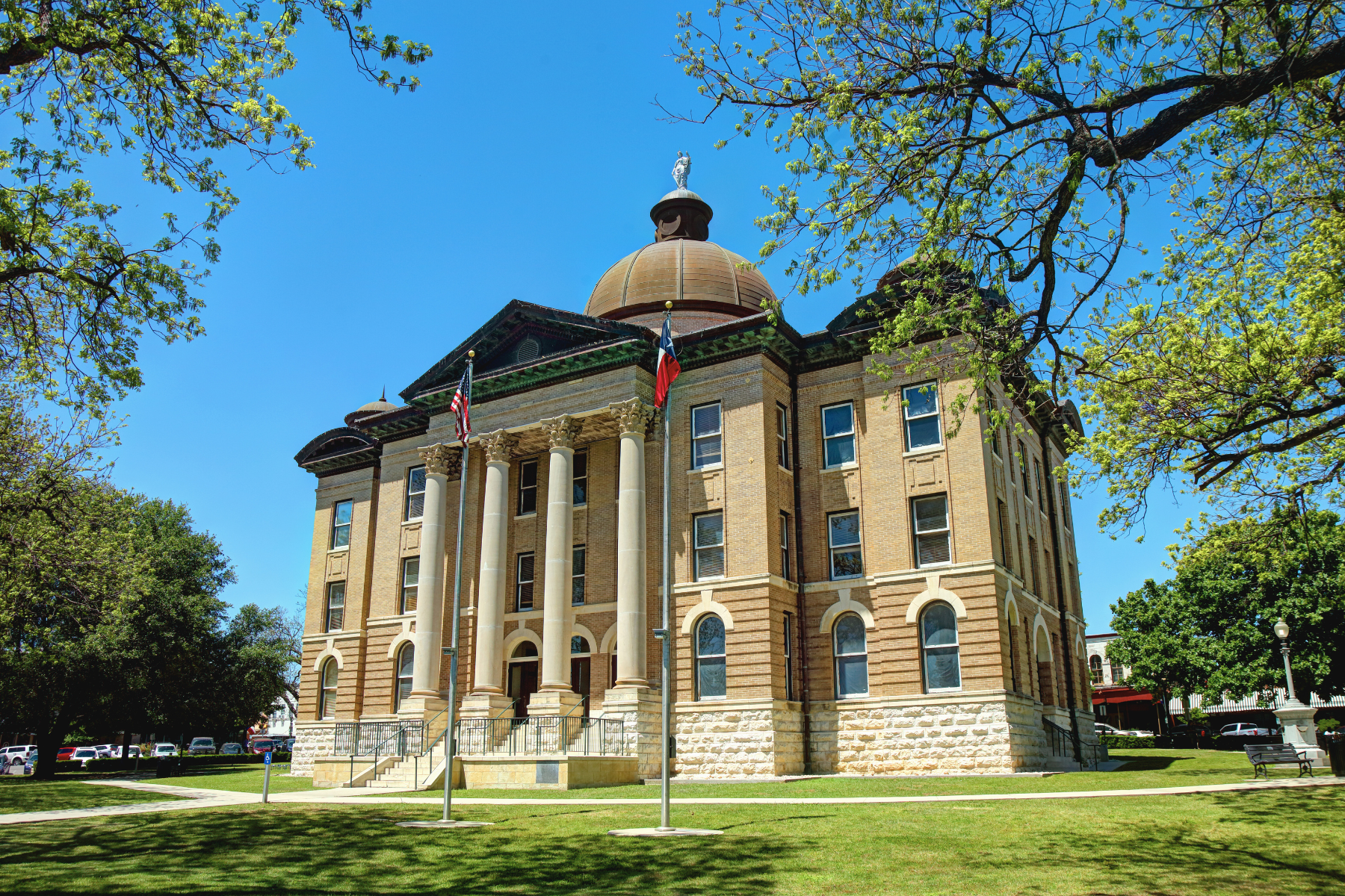 Nestled in the heart of San Marcos, the historic courthouse boasts a majestic domed roof and stately columns, surrounded by lush trees and fluttering flags, under a clear blue sky—an iconic backdrop for any local DWI lawyer.