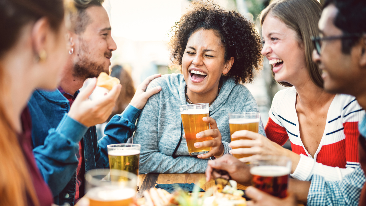 Five people are sitting and laughing together around a table in Texas, enjoying several glasses of beer and snacks, all while being mindful of the legal alcohol limit.