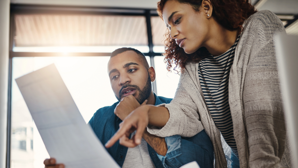 In a Texas office setting, two people review a document together; one is sitting and holding the paper, while the other stands and points at it, discussing which crimes have been expunged.