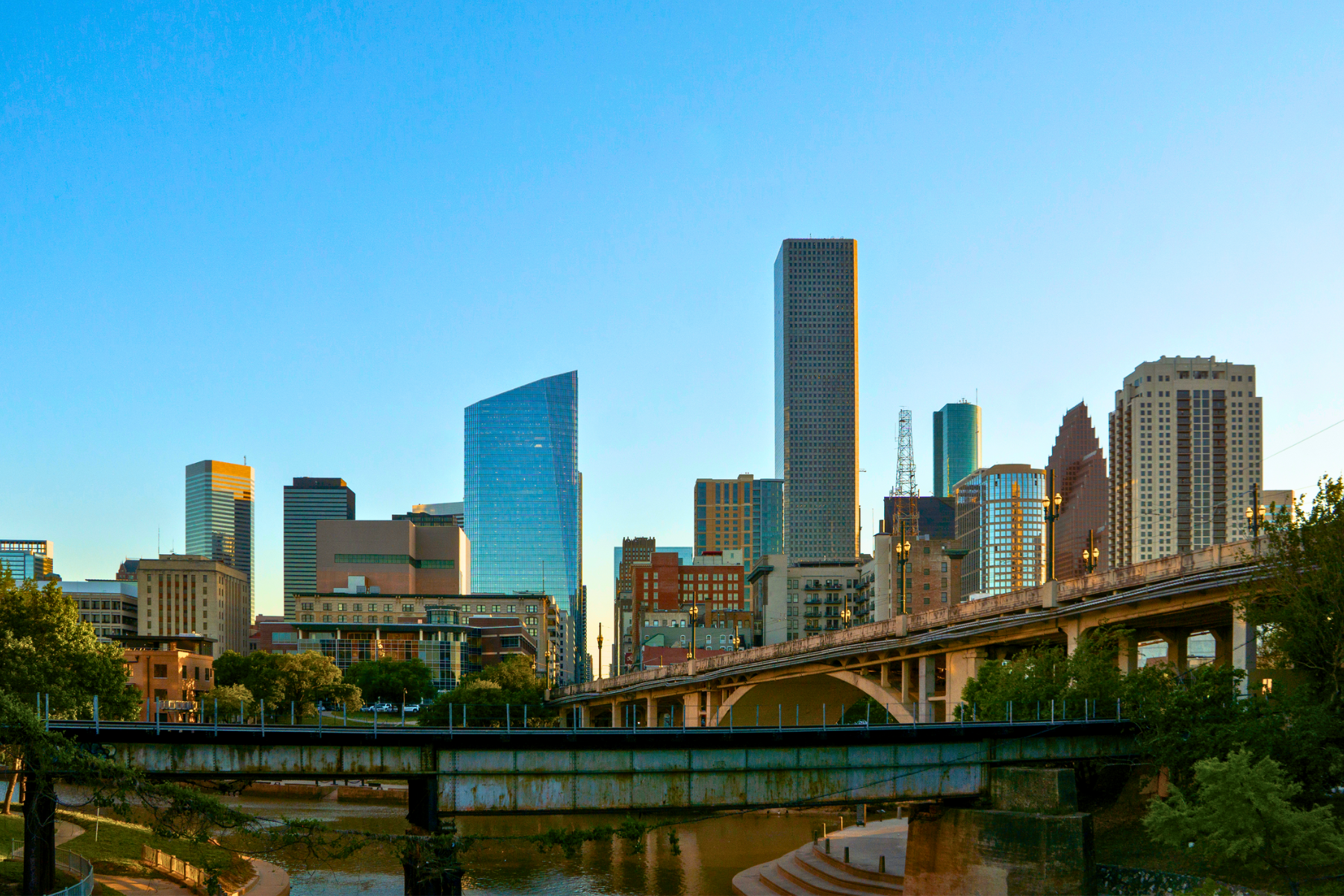 The skyline of a city with modern skyscrapers rises majestically, while a prominent bridge in the foreground reflects progress under a clear blue sky. Just like navigating this view, finding the right Houston DWI Lawyer can guide you through complex legal landscapes.